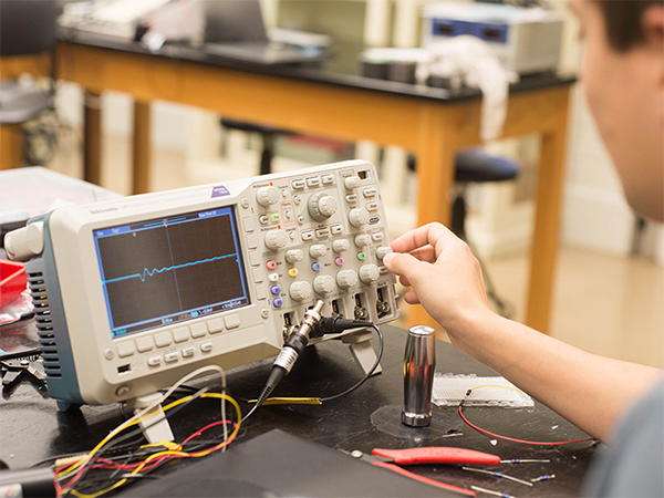 A student turns the knobs on a device in a physics lab.